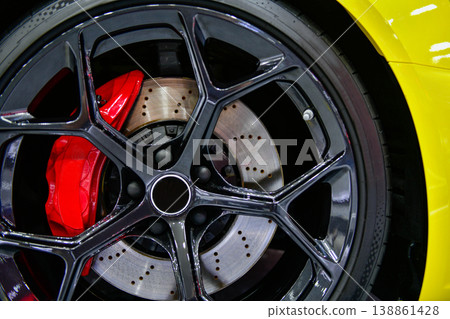 Close-up of a high-performance sports car black alloy wheel with red brake calipers and drilled brake discs on a yellow vehicle. 138861428