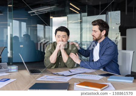 Male colleague offers empathetic support to stressed asian businessman at his office desk, consoling him during a moment of anxiety, burnout and workplace distress Male colleague offers empathetic support to stressed asian businessman at his office desk, consoling him during a moment of anxiety, burnout and workplace distress 138861570