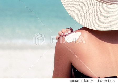Woman applying sunscreen creme on  tanned  shoulder. Skincare. Sun protection sun cream. Bikini hat woman applying sunscreen lotion on back 138861810
