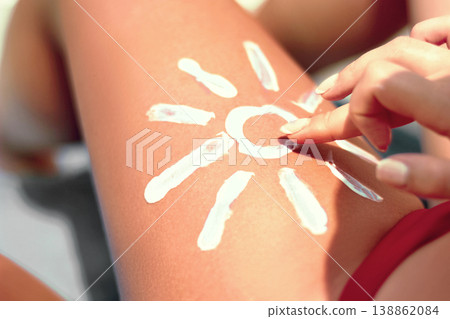 Sunbath protection. Woman using Suntan Lotion At The Beach In Form Of The Sun on leg Sunbath protection. Woman using Suntan Lotion At The Beach In Form Of The Sun on leg 138862084