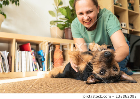 Woman playing with her pet dog on the carpet at home, enjoying a moment of companionship and happiness. Caring and loving pets. A happy moment in life Woman playing with her pet dog on the carpet at home, enjoying a moment of companionship and happiness. Caring and loving pets. A happy moment in life 138862092