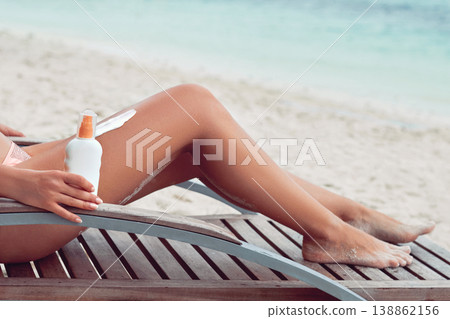 Young woman applying sunscreen lotion, holding sun cream bottle on the beach. Sun protection. Skin care 138862156