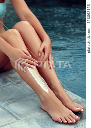 Beautiful legs outdoors by pool under sunshine on summer day. Woman apply sun protection cream on her smooth tanned legs. Skincare. Sunscreen on Feet 138862158