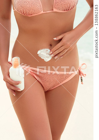Young woman applying sunscreen lotion, holding sun cream bottle on the beach. Sun protection Young woman applying sunscreen lotion, holding sun cream bottle on the beach. Sun protection 138862163