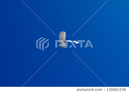 Skydiver parachutist descending with white parachute and white flag against clear blue sky Skydiver parachutist descending with white parachute and white flag against clear blue sky 138862336