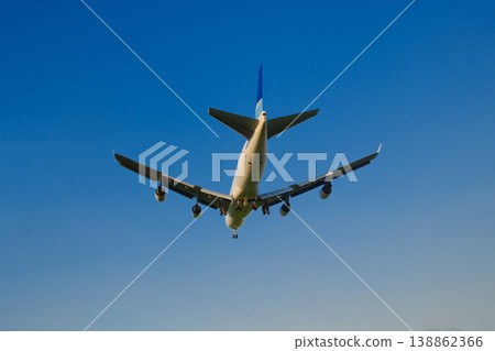 Large wide body commercial jet airplane flying against deep blue sky viewed from below at airfield Large wide body commercial jet airplane flying against deep blue sky viewed from below at airfield 138862366
