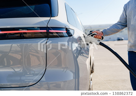 Person charging electric car at a charging station in daylight Person charging electric car at a charging station in daylight 138862372