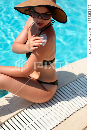 Pretty Woman Applying Sunscreen On Shoulder Sitting By Poolside Close View In Summer Sunlight. Skincare And Sun Protection Concept With Healthy Skin Glow Pretty Woman Applying Sunscreen On Shoulder Sitting By Poolside Close View In Summer Sunlight. Skincare And Sun Protection Concept With Healthy Skin Glow 138863141