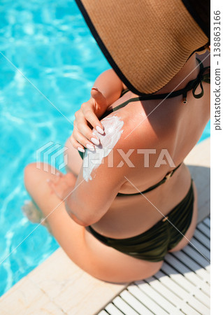 Top View Of Woman Applying Sunscreen On Shoulder Sitting By Poolside In Bright Summer Light. Skincare And Sun Protection Concept Top View Of Woman Applying Sunscreen On Shoulder Sitting By Poolside In Bright Summer Light. Skincare And Sun Protection Concept 138863166