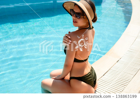 Beautiful Woman Sitting by Pool with Sunscreen on Back. Summer Skincare and Sun Protection Concept 138863199