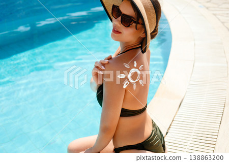 Beautiful Woman with Sunscreen on Back Sitting by Pool. Skincare Routine and Sun Protection Concept Beautiful Woman with Sunscreen on Back Sitting by Pool. Skincare Routine and Sun Protection Concept 138863200