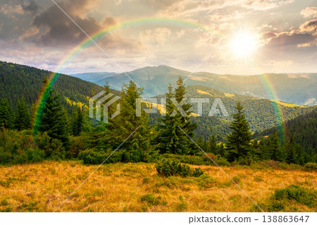 sunset over hillside of mountain range with coniferous forest and grassy meadow. beautiful summer landscape with alp. wonderful nature background of highland under rainbow for earth day 138863647