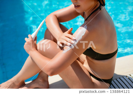 Woman Applying Sunscreen On Shoulder Sitting By Poolside Close View In Summer Sunlight With Clear Water Background Woman Applying Sunscreen On Shoulder Sitting By Poolside Close View In Summer Sunlight With Clear Water Background 138864121