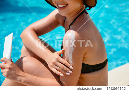 Woman Smiling And Applying Sunscreen On Shoulder Sitting By Poolside In Summer Sunlight With Relaxed Lifestyle Mood 138864122