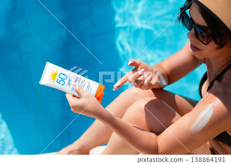 Top View Of Woman Holding Sunscreen Bottle And Applying Cream On Shoulder Sitting By Poolside In Bright Sunlight Top View Of Woman Holding Sunscreen Bottle And Applying Cream On Shoulder Sitting By Poolside In Bright Sunlight 138864191