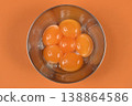 Raw Egg Yolks in Metal Bowl on Orange Background 138864586