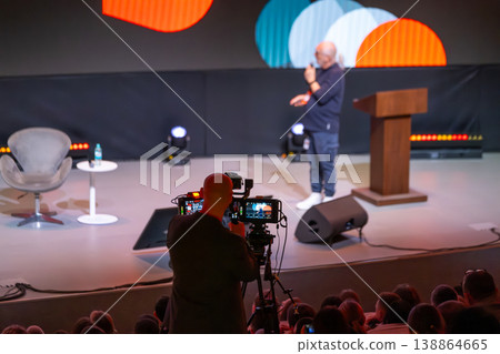 Videographer recording speaker on stage during conference presentation with audience  138864665