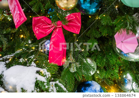 large shiny pink bow sits among green pine branches with metallic blue, silver, and gold ornaments, an origami umbrella, and warm fairy lights large shiny pink bow sits among green pine branches with metallic blue, silver, and gold ornaments, an origami umbrella, and warm fairy lights 138864674