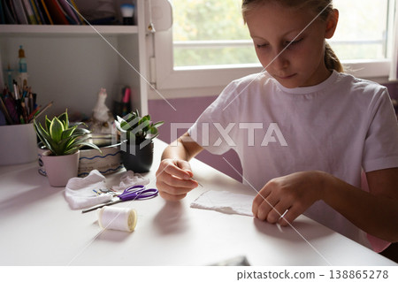 girl sits at a white table sewing white fabric with a needle diy girl sits at a white table sewing white fabric with a needle diy 138865278