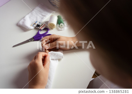 kid hands sew white fabric with needle and thread on light table with purple scissors and spools crafting hobby diy creative 138865281