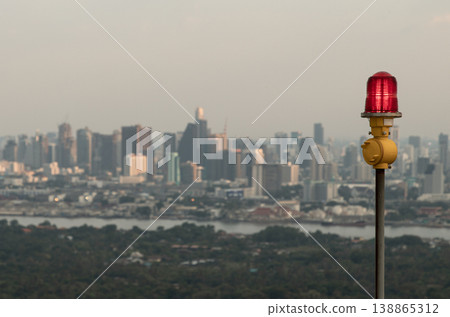 Standing as a solitary sentinel, a vibrant red obstruction light glows or aircraft warning light atop a slender yellow pole, its watchful radiance serving as a vital aeronautical beacon to ensure Standing as a solitary sentinel, a vibrant red obstruction light glows or aircraft warning light atop a slender yellow pole, its watchful radiance serving as a vital aeronautical beacon to ensure 138865312