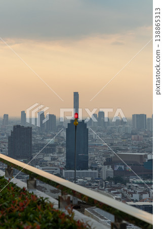 A singular crimson aircraft warning light stands as a silent sentinel atop a high-rise, overlooking a vast urban vista at the gentle threshold of dusk. As Bangkok unfolds in a dense tapestry of A singular crimson aircraft warning light stands as a silent sentinel atop a high-rise, overlooking a vast urban vista at the gentle threshold of dusk. As Bangkok unfolds in a dense tapestry of 138865313