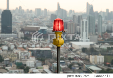 A singular crimson aircraft warning light (obstruction light) stands as a silent sentinel against the sprawling, muted tapestry of the metropolitan horizon. A singular crimson aircraft warning light (obstruction light) stands as a silent sentinel against the sprawling, muted tapestry of the metropolitan horizon. 138865315