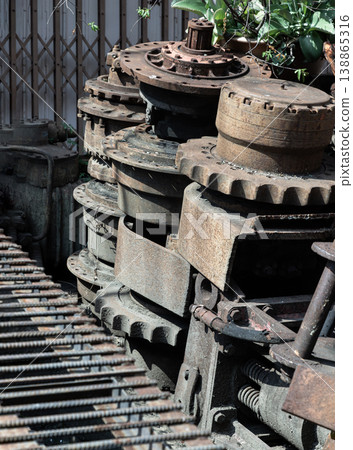 Within a sun-drenched sanctuary, weathered iron gears and machinery components rest in silent, stacked formations. These mechanical relics, etched with a patina of labor, reveal a rugged beauty 138865316