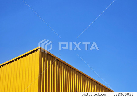 Modern industrial building with vibrant yellow corrugated metal walls set against a clear blue sky. Modern industrial building with vibrant yellow corrugated metal walls set against a clear blue sky. 138866035
