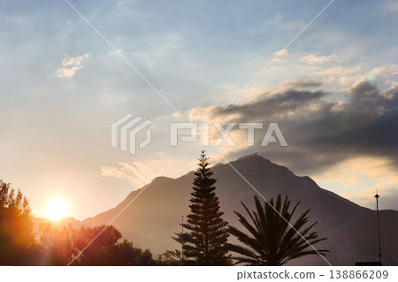 Golden sun setting behind mountains with palm trees Golden sun setting behind mountains with palm trees 138866209