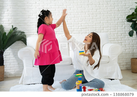 A mother shares a joyful moment with her autistic daughter in a cozy living room. Surrounded by colorful toys, the scene highlights neurodiversity, emotional bonding, and inclusive family life 138868079