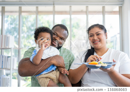 Happy family spending quality time feeding their baby in a bright home setting. Promotes healthy parenting, emotional bonding, and modern lifestyle through nurturing care and joyful interaction Happy family spending quality time feeding their baby in a bright home setting. Promotes healthy parenting, emotional bonding, and modern lifestyle through nurturing care and joyful interaction 138868083