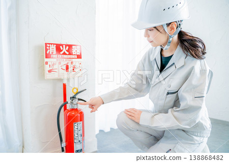 A woman in work clothes inspecting fire safety equipment. 138868482