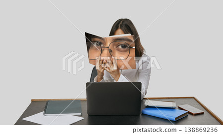 Young woman at desk with laptop holding printed face panel online identity metaphor Young woman at desk with laptop holding printed face panel online identity metaphor 138869236