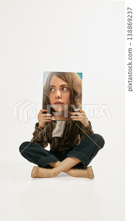 Young woman sitting cross legged holding printed face panel casual fashion studio portrait. Young woman sitting cross legged holding printed face panel casual fashion studio portrait. 138869237