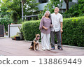 Two older adults enjoy a peaceful walk with their dog in a lush, suburban outdoor setting. The scene reflects active aging, pet companionship, emotional bonding, and a mindful lifestyle surrounded 138869449