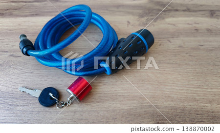 Strong blue cable lock with key stands on wood surface in bright light 138870002