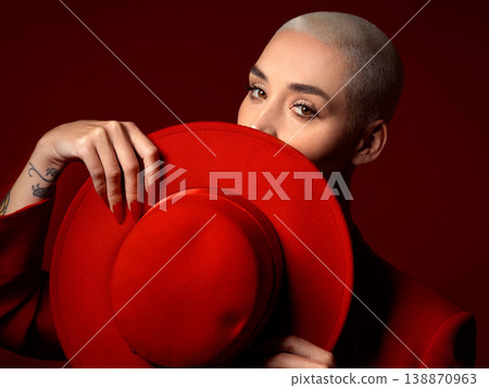 Portrait, fashion and hat with a woman on a red background in studio for elegant or trendy style. Face, hide and cover with a young female model looking edgy or classy in a suit or unique clothes Portrait, fashion and hat with a woman on a red background in studio for elegant or trendy style. Face, hide and cover with a young female model looking edgy or classy in a suit or unique clothes 138870963