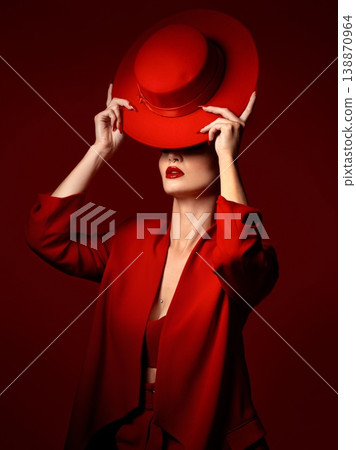 Hat, fashion and a model woman on a red studio background for elegant or trendy style. Aesthetic, art or confidence with a young female person in an edgy and classy outfit, suit or clothes for beauty Hat, fashion and a model woman on a red studio background for elegant or trendy style. Aesthetic, art or confidence with a young female person in an edgy and classy outfit, suit or clothes for beauty 138870964