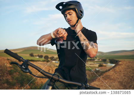 Sports, bike and man checking his pulse on a mountain dirt road in nature for race or competition training. Fitness, exercise and young male biker athlete with watch for the time at an outdoor trail. 138871085