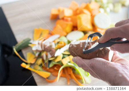 Peeling potato with peeler during vegetable preparation in kitchen 138871164