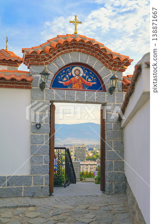 Plovdiv church gate with stone arch and religious icon overlooking cityscape through entrance of Saints Archangels church in Plovdiv Bulgaria. Concept of religion heritage, travel culture 138871667