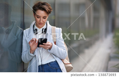 Woman, smartphone and social media with communication outdoor, chat or email with headphones, travel to work and mockup space. Young creative in city, mobile app with technology and 5g in Boston 138871693
