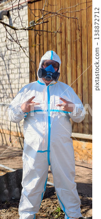 Person in disposable hazmat suit, respirator and goggles stands outdoors making double peace signs, conveying ppe safety, positivity and hope during pandemic and disinfection work. Person in disposable hazmat suit, respirator and goggles stands outdoors making double peace signs, conveying ppe safety, positivity and hope during pandemic and disinfection work. 138872712