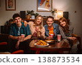 Friends enjoying tasty snacks and drinks in a cozy living room, making memories and friendship. 138873534