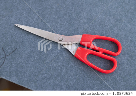 Red-handled scissors on gray felt fabric surface Red-handled scissors on gray felt fabric surface 138873624