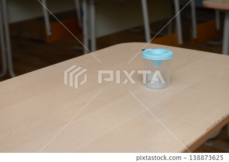 Empty classroom desk with blue-topped plastic cup on wooden table Empty classroom desk with blue-topped plastic cup on wooden table 138873625