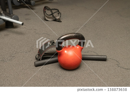 Red kettlebell on gym floor with wrist straps and protective goggles nearby 138873638
