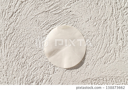 Round paper on textured white wall in sunlight Round paper on textured white wall in sunlight 138873662