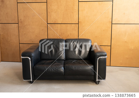Black leather two seat sofa placed against wooden panels Black leather two seat sofa placed against wooden panels 138873665